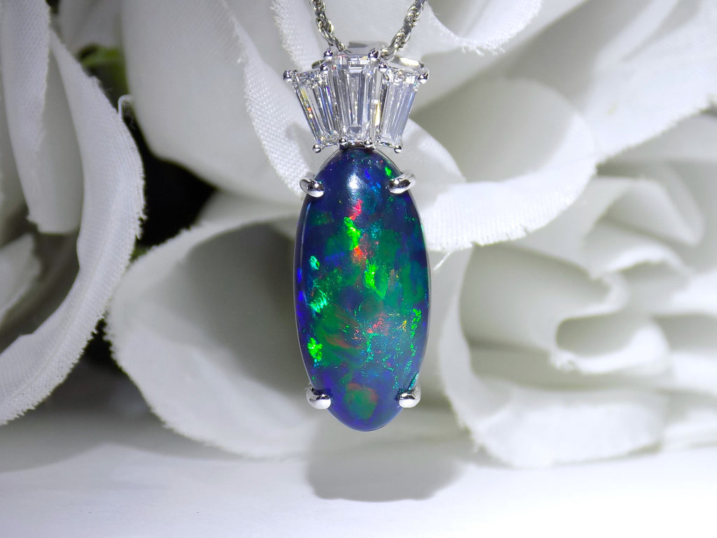 This is a women's 7.48ct total weight natural black opal and baguette diamond pendant or necklace in white gold shown with a flowery background.