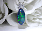 This is a women's 7.48ct total weight natural black opal and baguette diamond pendant or necklace in white gold shown with a flowery background.