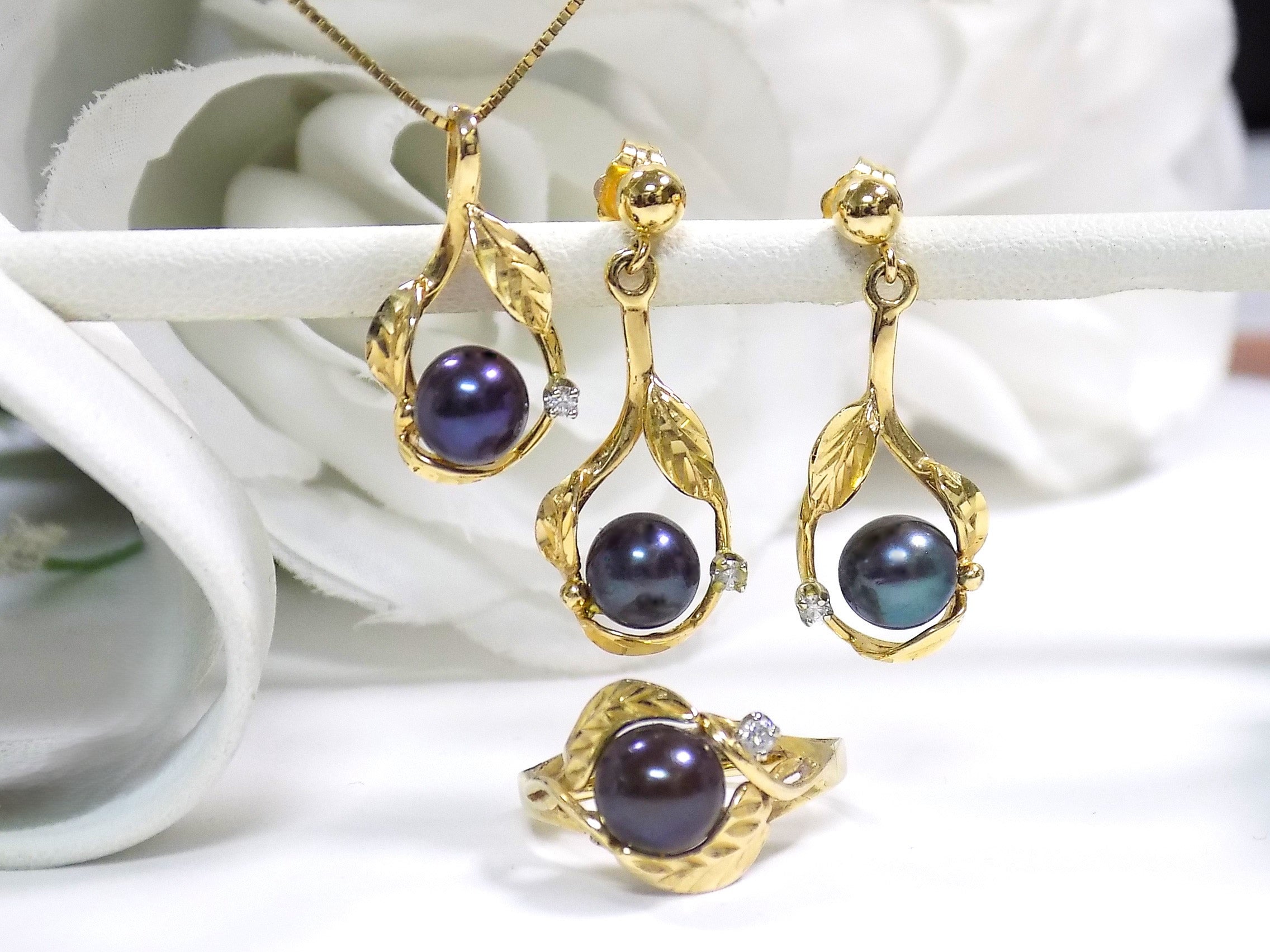 This a set of genuine black pearl ring, earrings and pendant in yellow gold from our estate collection fully restored to like new condition with a white gold background.