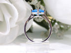 This is a diagonally set natural 2.50ct cushion cut blue topaz and .10ct diamond accents in 10K white gold side view with a white floral background.