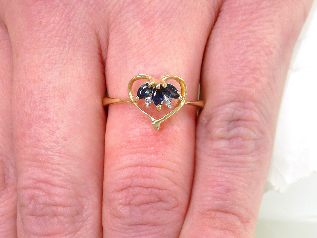 This is an estate natural marquise shaped London blue and diamond heart shape ring in 10K yellow gold on a woman's finger.