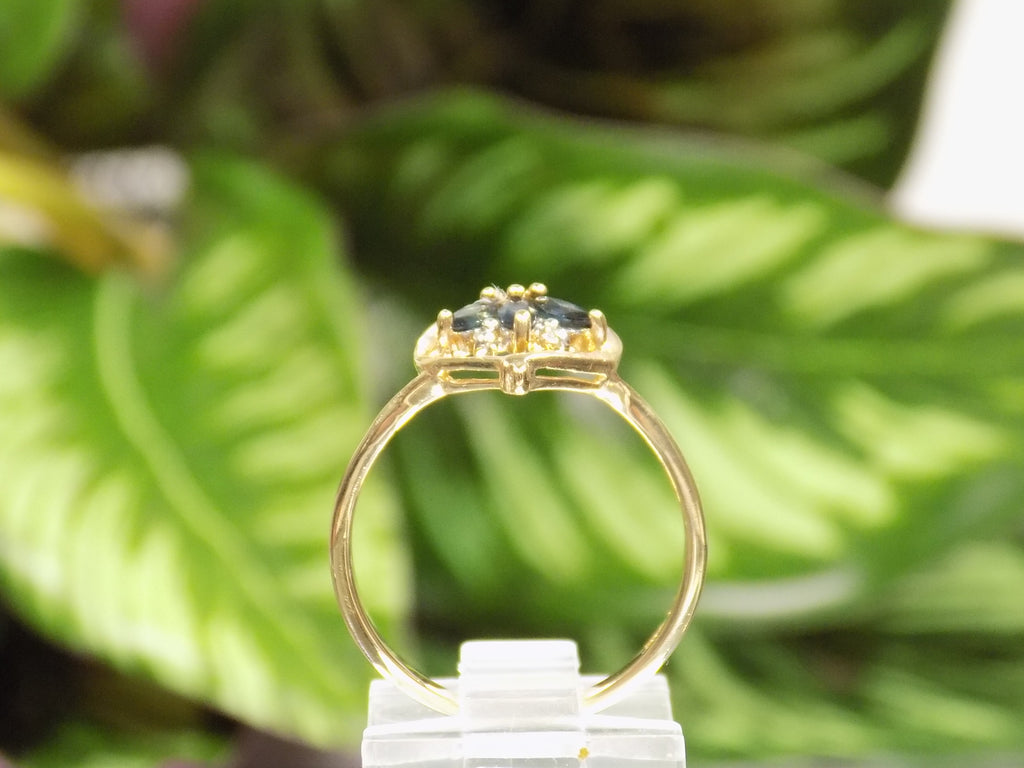 This is an estate natural marquise shaped London blue and diamond heart shape ring in 10K yellow gold side view on a mirrored surface with a green leaf background.