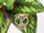 This is an estate natural marquise shaped London blue and diamond heart shape ring in 10K yellow gold on a mirrored surface with a green leaf background.