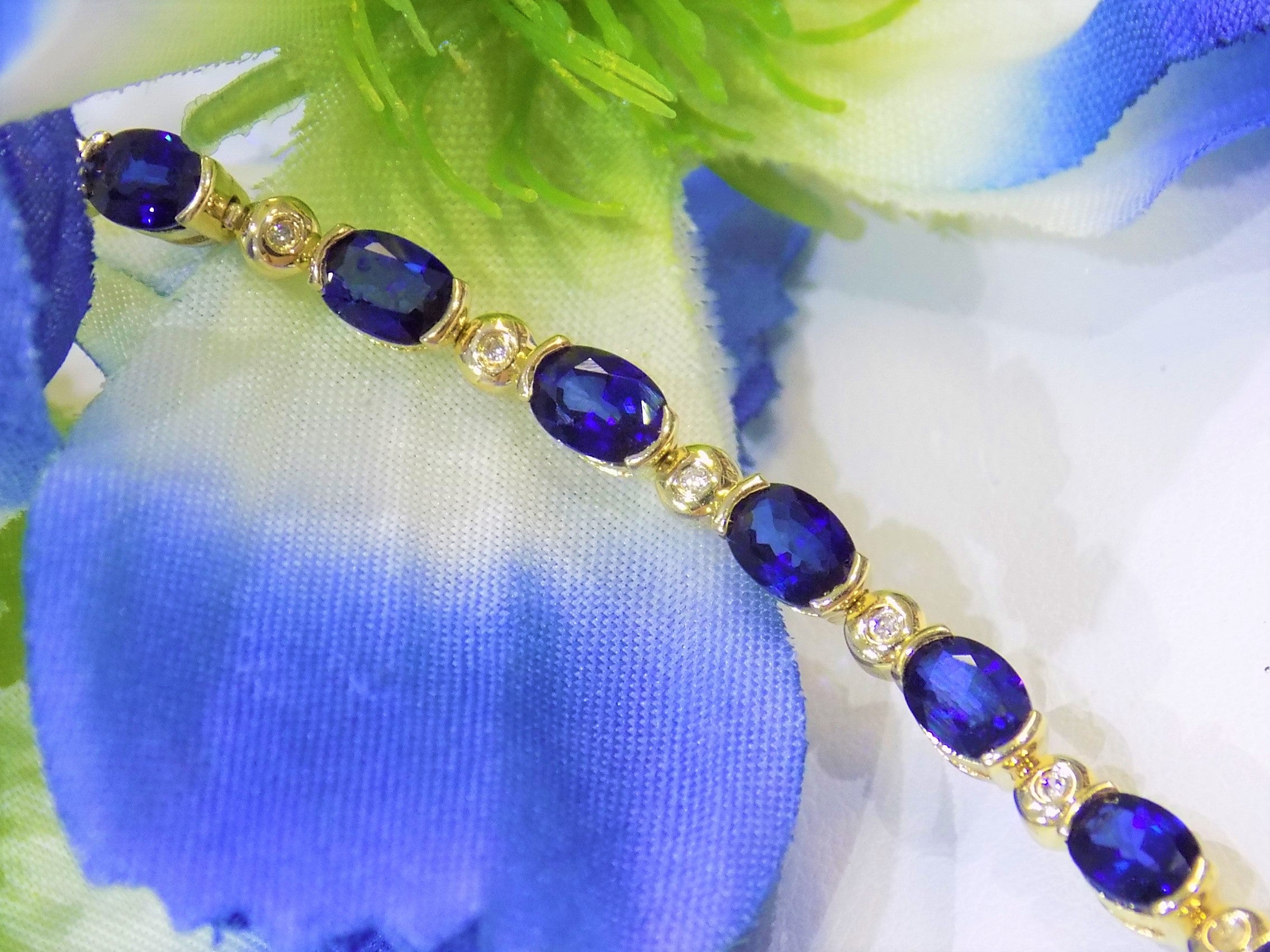 This is a women's bracelet with 10.00ct of natural oval shaped sapphires and round diamonds in 14K yellow gold with a blue. white, and green floral background.