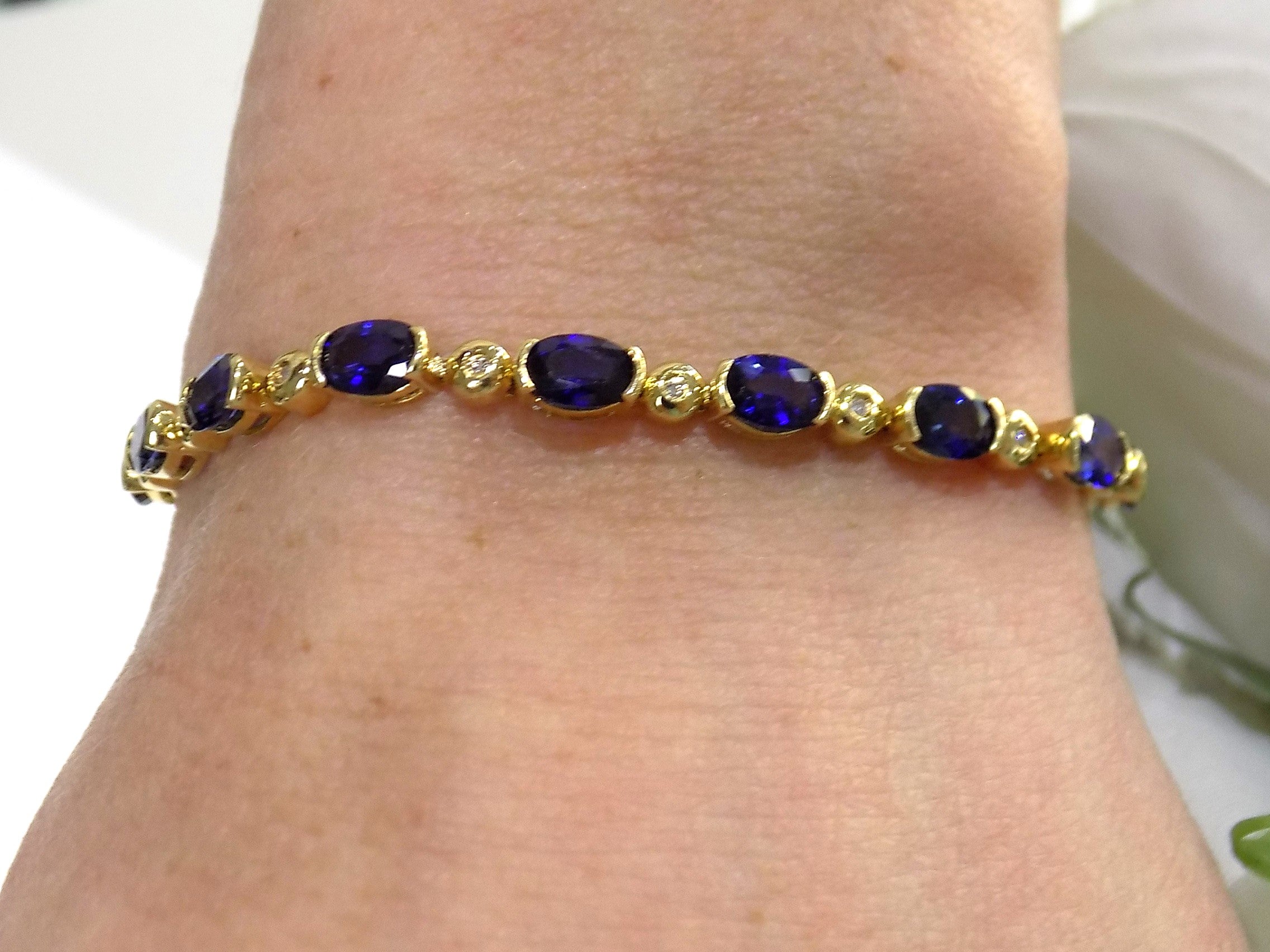 This is a women's bracelet with 10.00ct of natural oval shaped sapphires and round diamonds in 14K yellow gold on a ladies wrist with a white background.