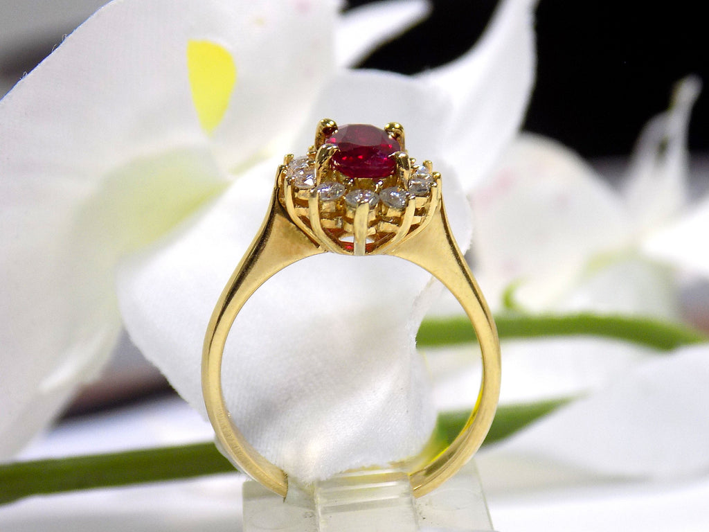This is a side view of a women's 1.46ct total natural GIA certified oval shape Burmese Ruby and diamond ring in 18K yellow gold shown with a white and green background. 