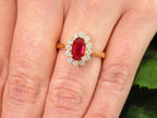This is women's 1.46ct total natural GIA certified oval shape Burmese Ruby and diamond ring in 18K yellow gold shown on a woman's finger.