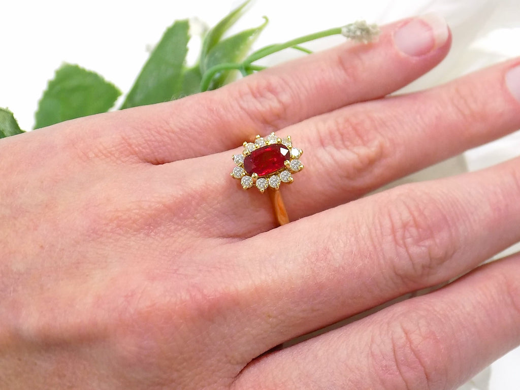 This is women's 1.46ct total natural GIA certified oval shape Burmese Ruby and diamond ring in 18K yellow gold shown on a woman's finger.