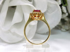 This is a side view of a women's 1.46ct total natural GIA certified oval shape Burmese Ruby and diamond ring in 18K yellow gold shown with a white and green background. 