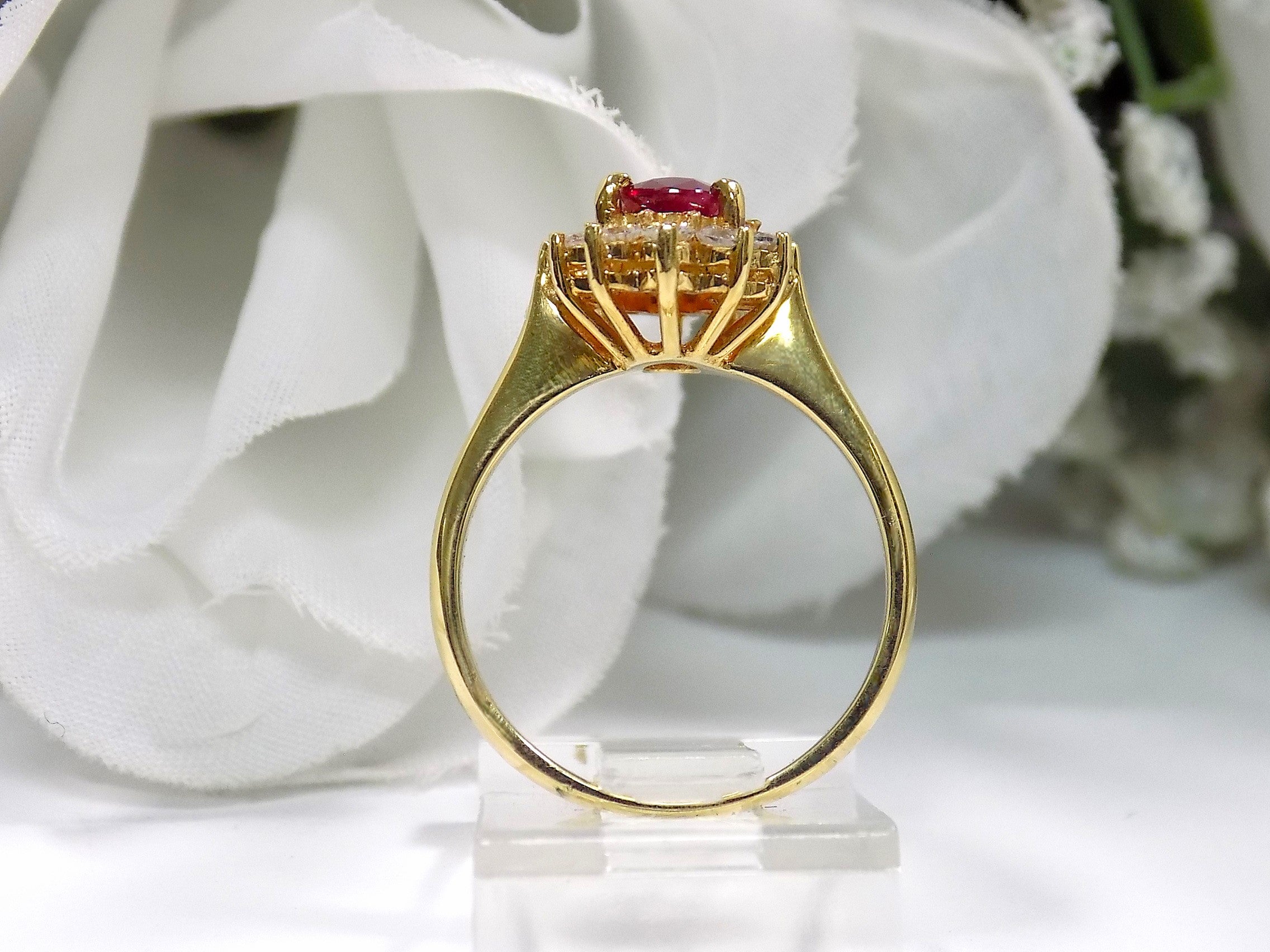 This is a side view of a women's 1.46ct total natural GIA certified oval shape Burmese Ruby and diamond ring in 18K yellow gold shown with a white and green background. 