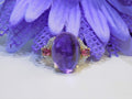 This is a women's natural 11.00ct cabochon shape amethyst with .20ct total weight natural pink tourmalines on either side plus .16ct total weight natural diamond accents on either side in 10K yellow gold with a purple floral background.