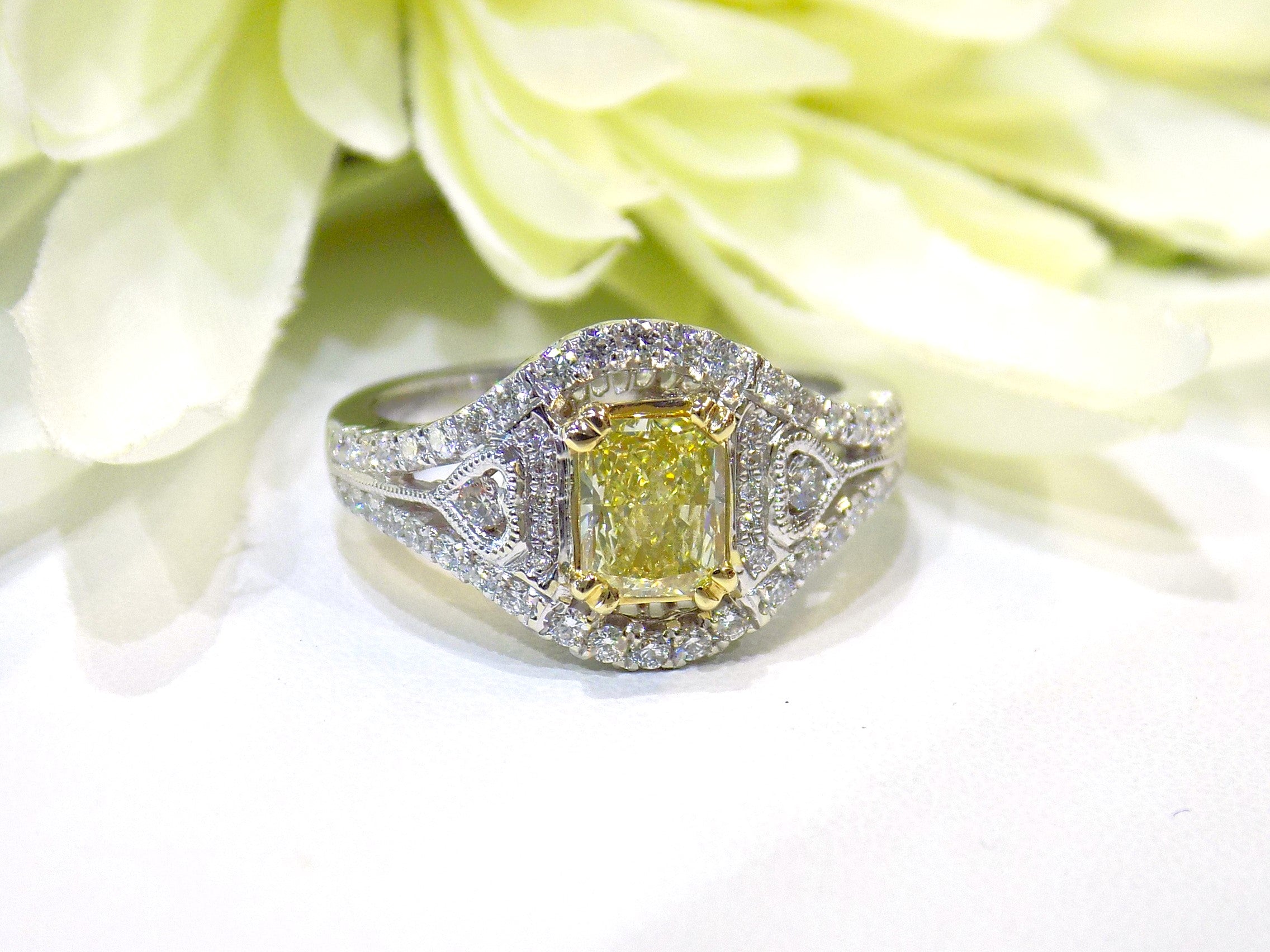 This is a 1.35ct total weight natural fancy yellow not enhanced diamond ring with white diamond accents in white gold with white flowery background.