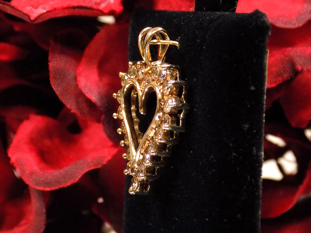 This is an estate heart shaped 1.00ct total weight natural champagne diamond pendant in 10K yellow gold side view on a black pad with a red floral background.