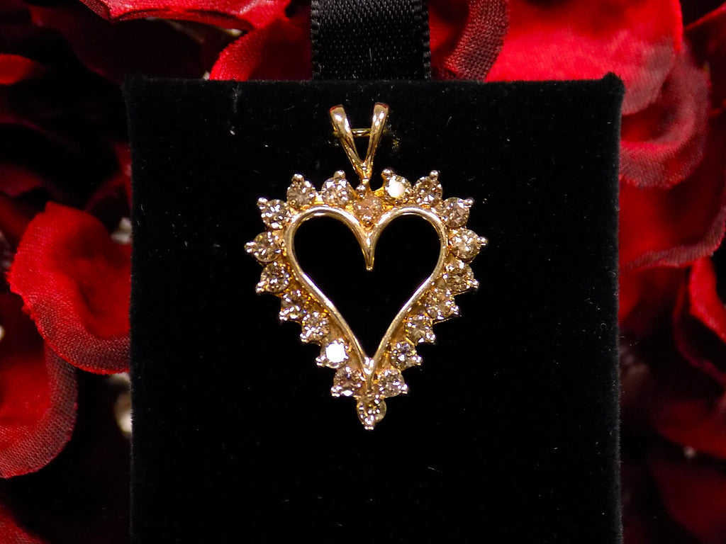 This is an estate heart shaped 1.00ct total weight natural champagne diamond pendant in 10K yellow gold on a black pad with a red floral background.