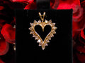 This is an estate heart shaped 1.00ct total weight natural champagne diamond pendant in 10K yellow gold on a black pad with a red floral background.
