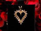 This is an estate heart shaped 1.00ct total weight natural champagne diamond pendant in 10K yellow gold on a black pad with a red floral background.