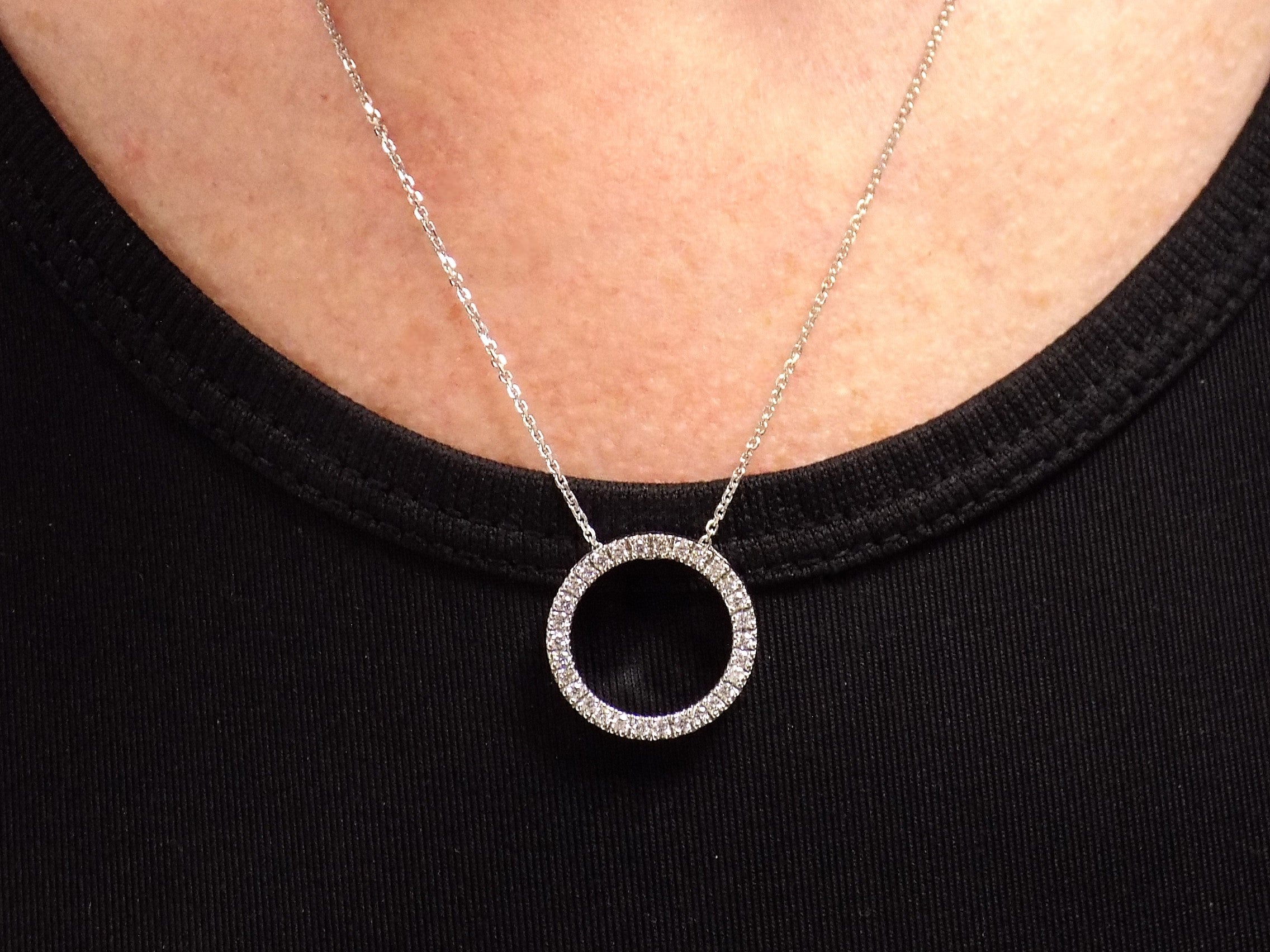 This is a circle .50ct natural diamond necklace with a cable style chain that can be adjusted in length of 14", 15", or 16" in 14K white gold displayed on a ladies neck with black shirt.