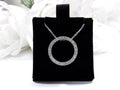This is a circle .50ct natural diamond necklace with a cable style chain that can be adjusted in length of 14", 15", or 16" in 14K white gold displayed on a black pad with a white floral background.