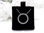 This is a circle .50ct natural diamond necklace with a cable style chain that can be adjusted in length of 14", 15", or 16" in 14K white gold displayed on a black pad with a white floral background.