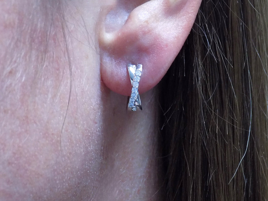This is a pair of criss-cross huggie diamond earrings in white gold in a woman's ear.
