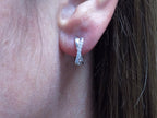 This is a pair of criss-cross huggie diamond earrings in white gold in a woman's ear.