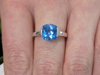 This is a tension set or channel set 4.00ct natural cushion cut blue topaz solitaire ring in 14K white gold on a ladies finger.