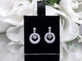 These are 1.34ct total weight natural round brilliant dancing diamond circle earrings in 14K white gold on a black pad with a floral background.