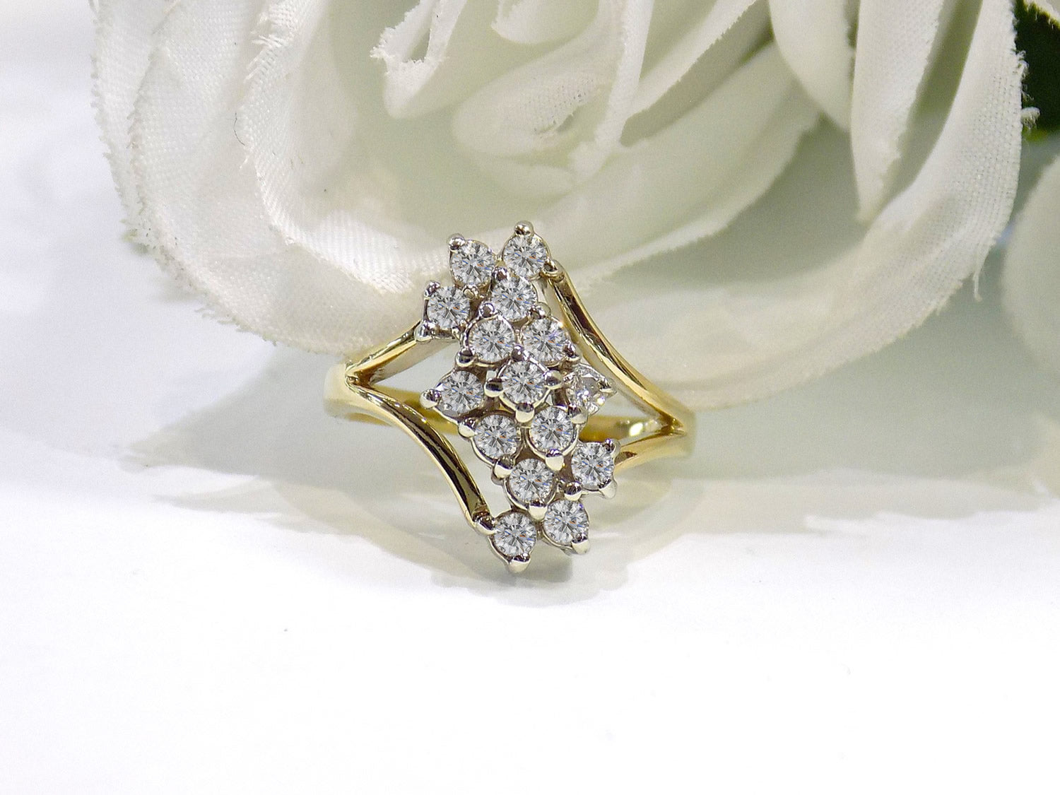 This is a 1ct total weight natural diamond waterfall style cluster ring in yellow gold with a white flowery background.