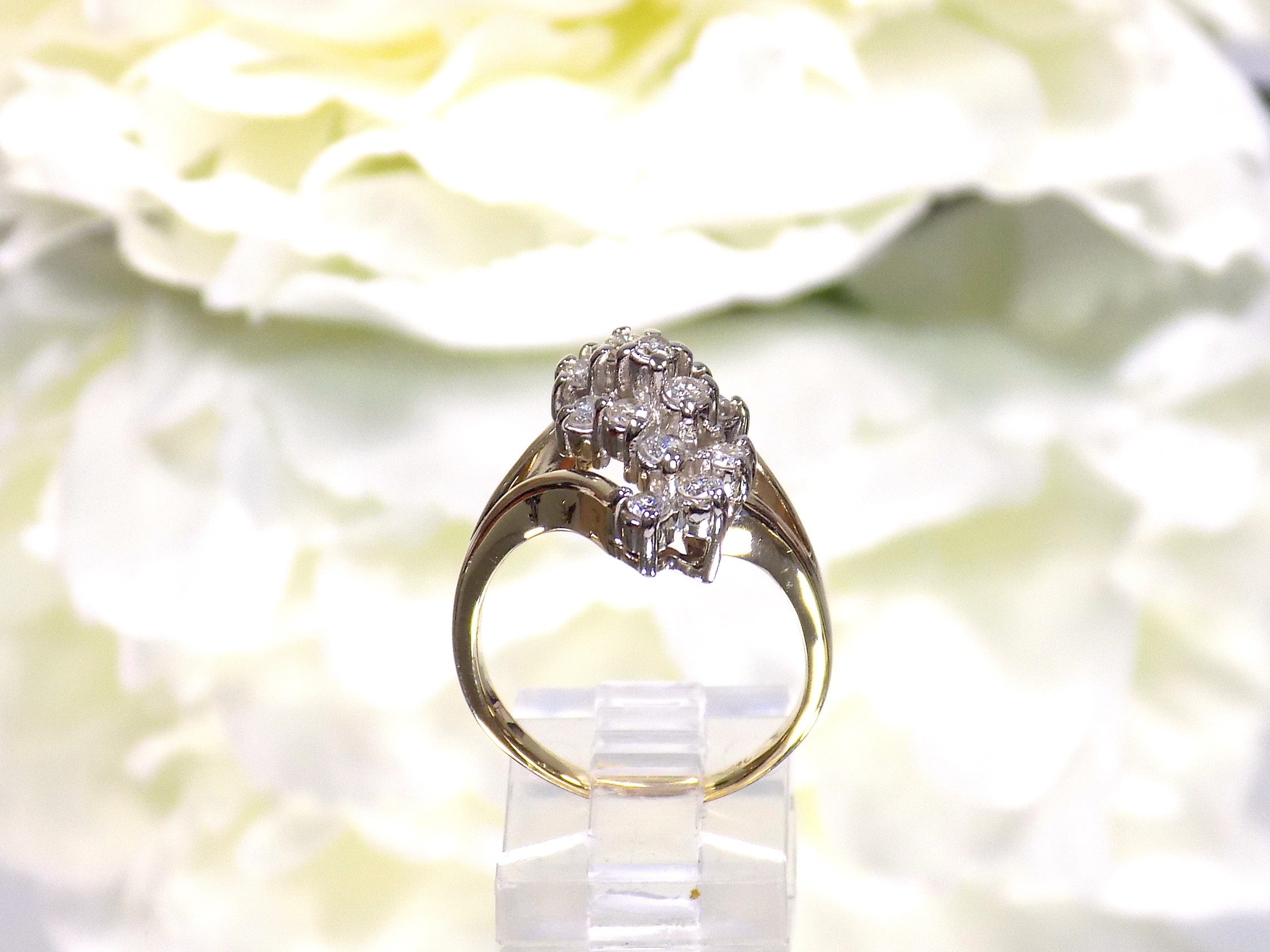 This is a side view of a 1ct total weight natural diamond waterfall style cluster ring in yellow gold with a white flowery background.