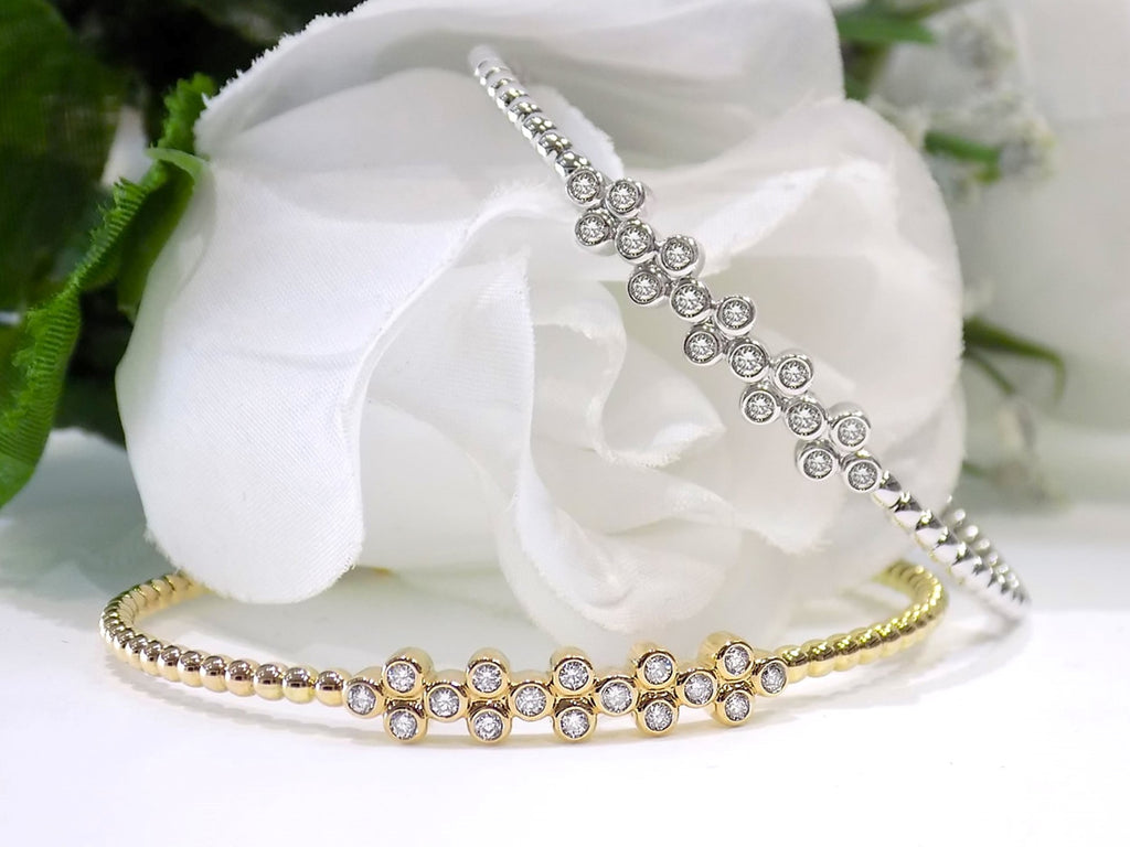 This is 2 women's.50ct total weight diamond flex bangle in one in 10K yellow gold and one in 10K white gold on a white and green floral background.