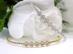 This is 2 women's.50ct total weight diamond flex bangle in one in 10K yellow gold and one in 10K white gold on a white and green floral background.