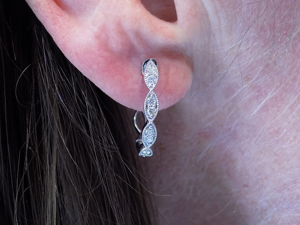 This is a pair of scalloped diamond hoop earrings in white gold shown in a ladies ear.