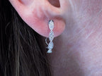 This is a pair of scalloped diamond hoop earrings in white gold shown in a ladies ear.