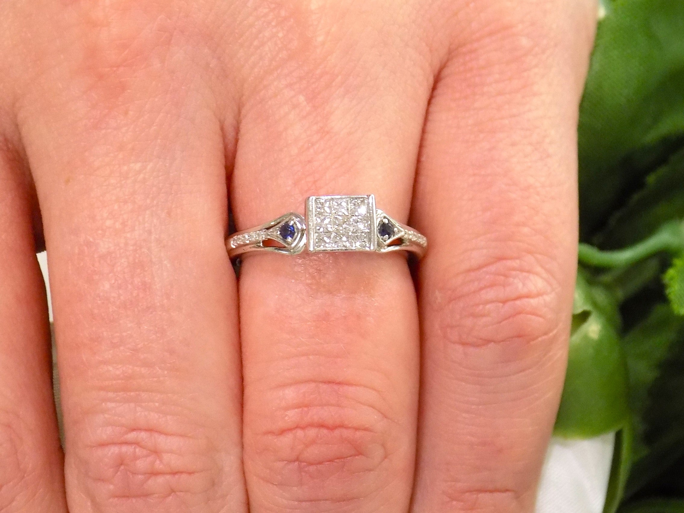 This is a Princess Cut Invisible Set Natural Diamond Ring with Round Sapphires in White Gold on a ladies finger.