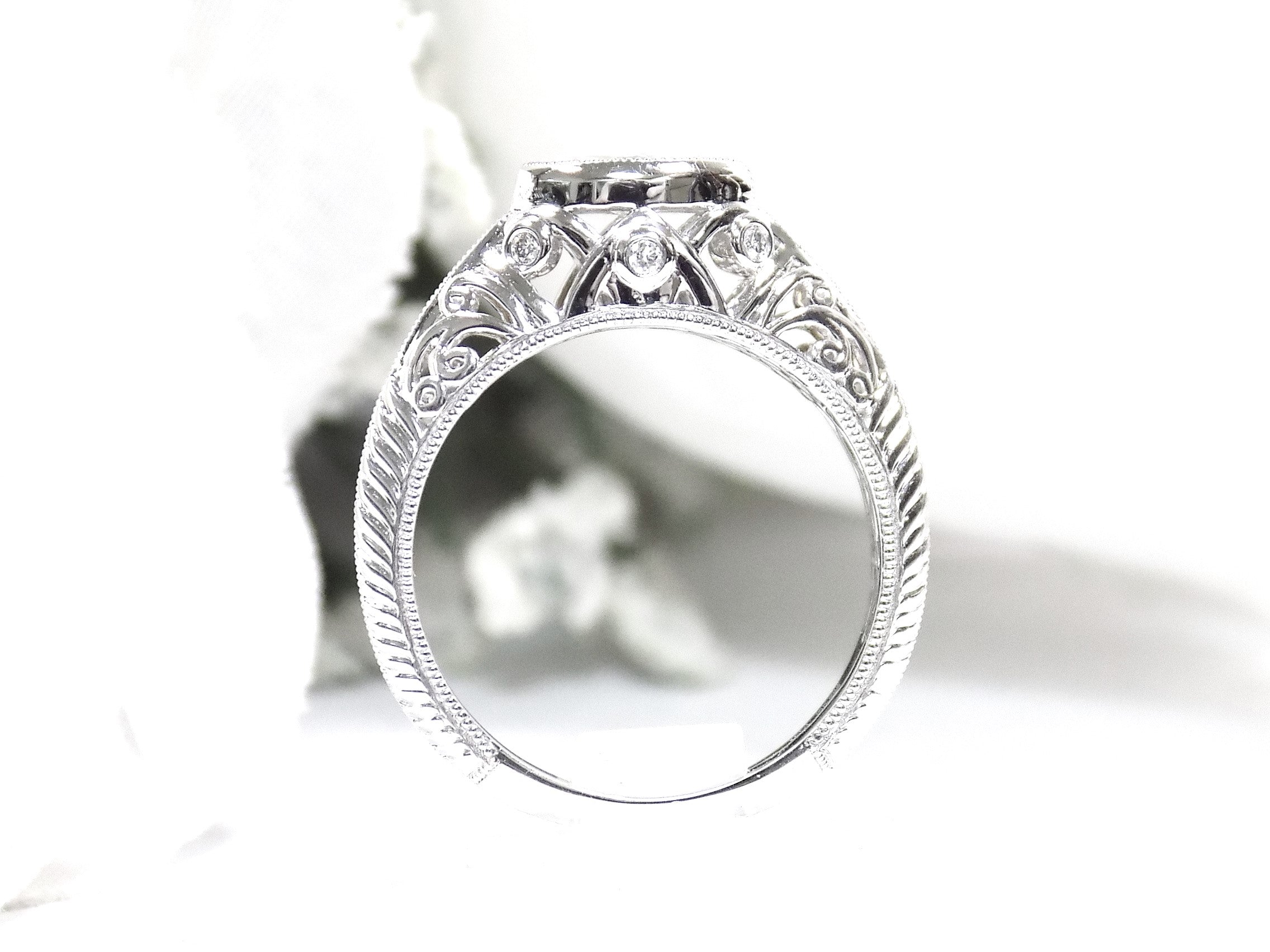 This is a bezel set marquise shape diamond set sideways in a white gold filigree ring shown from the side with a white background.