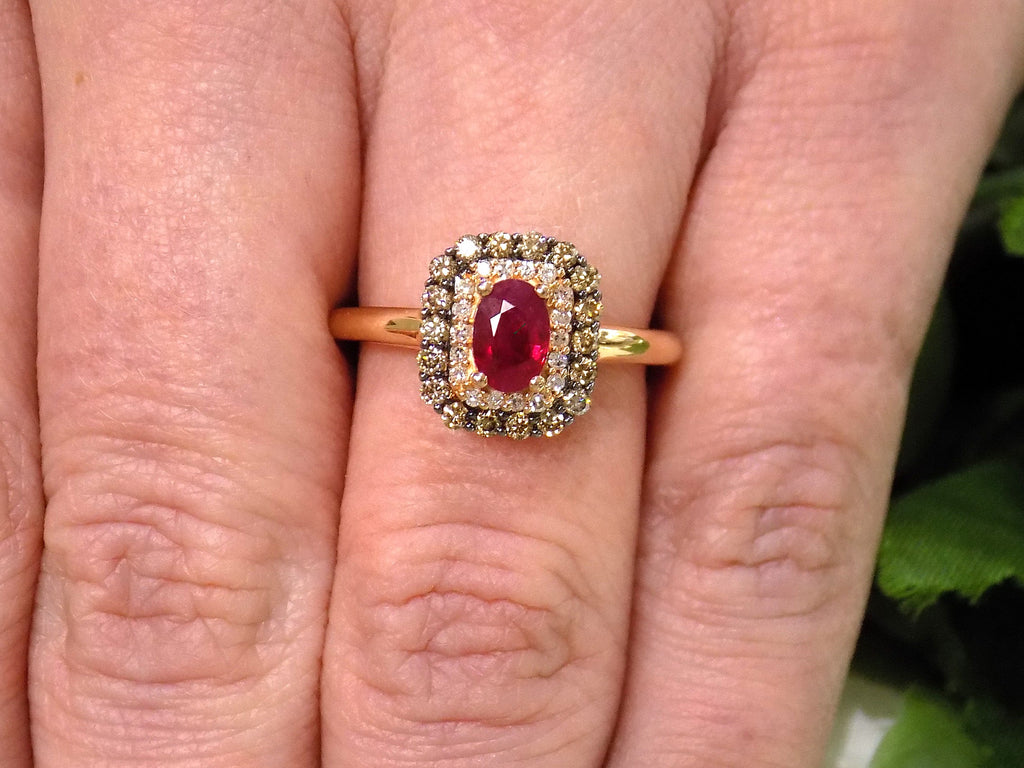 This is a women's effy brand ring with a .57ct natural oval shape ruby with a halo of natural white diamonds and a halo of chocolate diamonds on the outside for a total wight of .43ct in diamonds set in 14K rose gold on a women's finger.