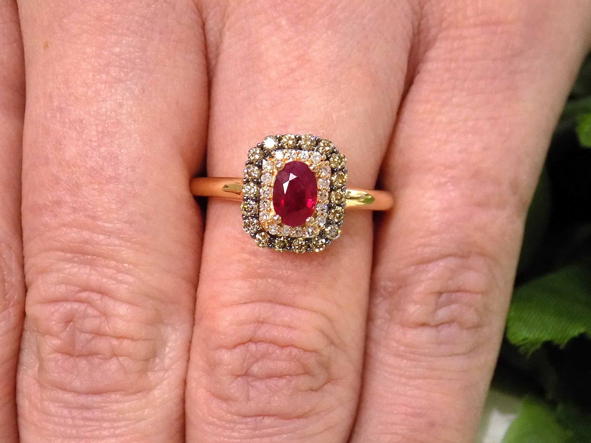 This is a women's effy brand ring with a .57ct natural oval shape ruby with a halo of natural white diamonds and a halo of chocolate diamonds on the outside for a total wight of .43ct in diamonds set in 14K rose gold on a women's finger.