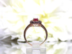 This is a women's effy brand ring with a .57ct natural oval shape ruby with a halo of natural white diamonds and a halo of chocolate diamonds on the outside for a total wight of .43ct in diamonds set in 14K rose gold with a white floral background in a side view.
