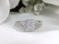 This is a .75ct natural emerald cut halo style ring with infinity style band in white gold with rose gold accents on the sides with a white background.