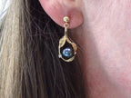 This is a pair of genuine black pearl earrings in yellow gold shown in a woman's ear.