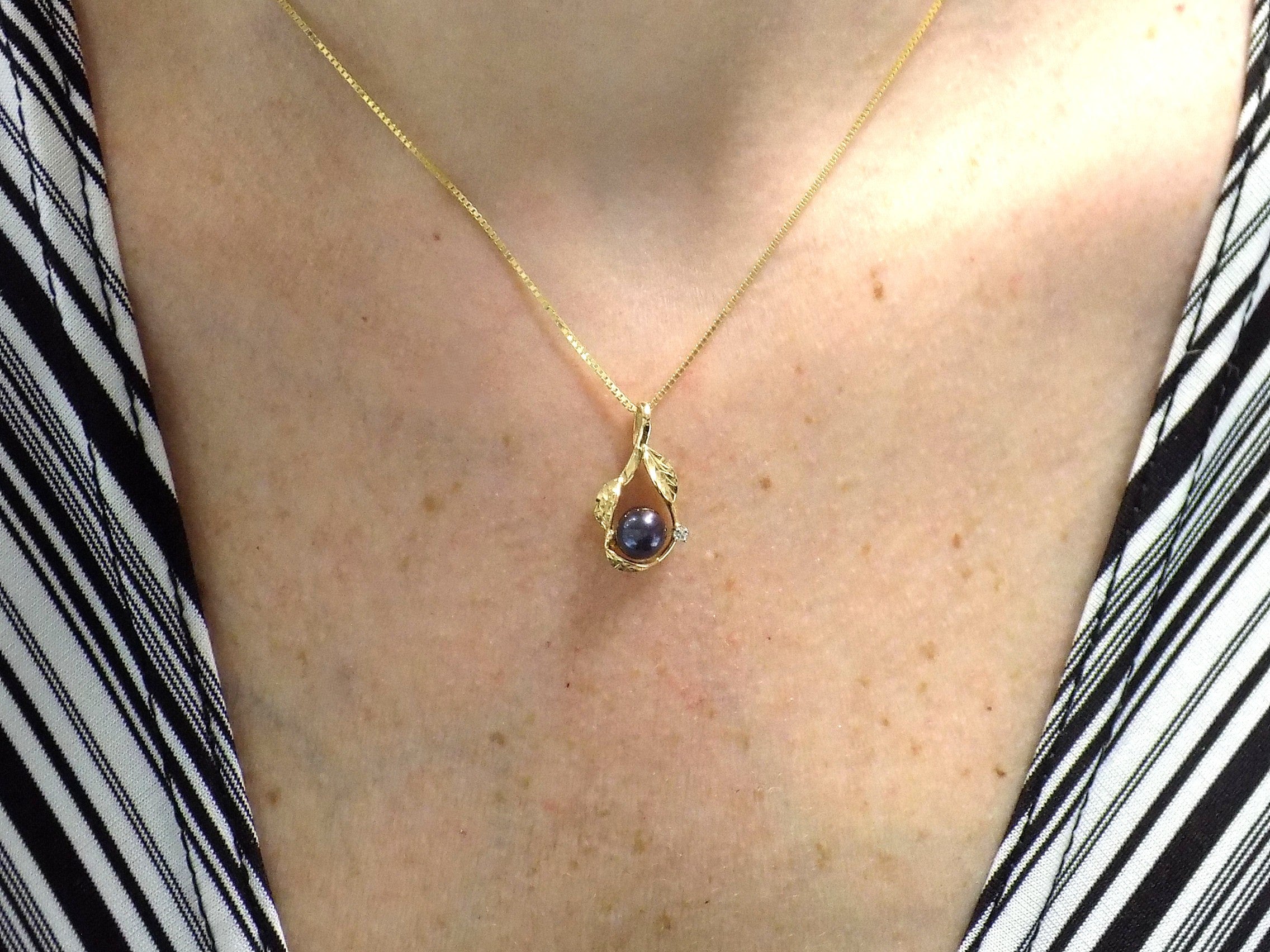 This is a fully restored to like new leafy designed black pearl and diamond pendant in yellow gold shown on woman's neck.