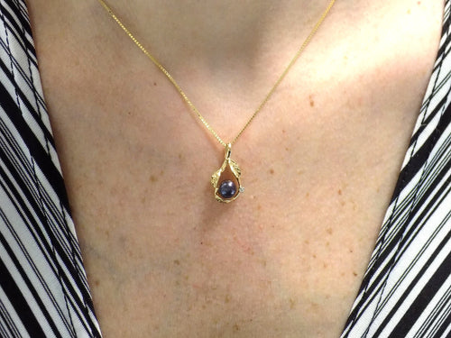 This is a fully restored to like new leafy designed black pearl and diamond pendant in yellow gold shown on woman's neck.