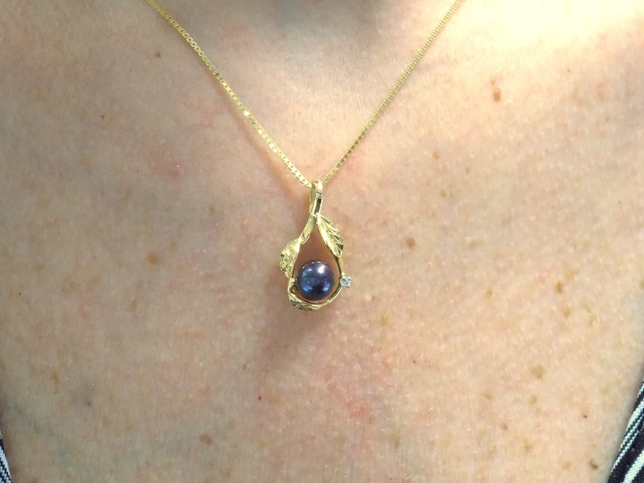 This is a fully restored to like new leafy designed black pearl and diamond pendant in yellow gold shown on woman's neck.