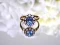 This a ring with an oval blue topaz in the center and surrounded by natural opals in yellow gold from our estate collection with a mirrored flowery background.