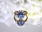 This a ring with an oval blue topaz in the center and surrounded by natural opals in yellow gold from our estate collection with a mirrored flowery background.