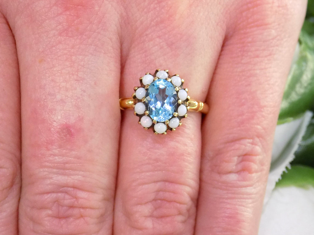 This a ring with an oval blue topaz in the center and surrounded by natural opals in yellow gold from our estate collection shown on a woman's finger.