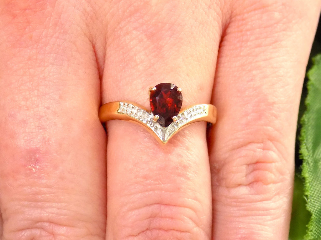 This is a pear shape garnet ring with diamond accents in yellow gold with shown on women's finger.