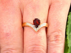This is a pear shape garnet ring with diamond accents in yellow gold with shown on women's finger.