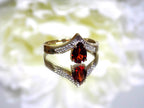 This is a pear shape garnet ring with diamond accents in yellow gold with flowery mirrored background.