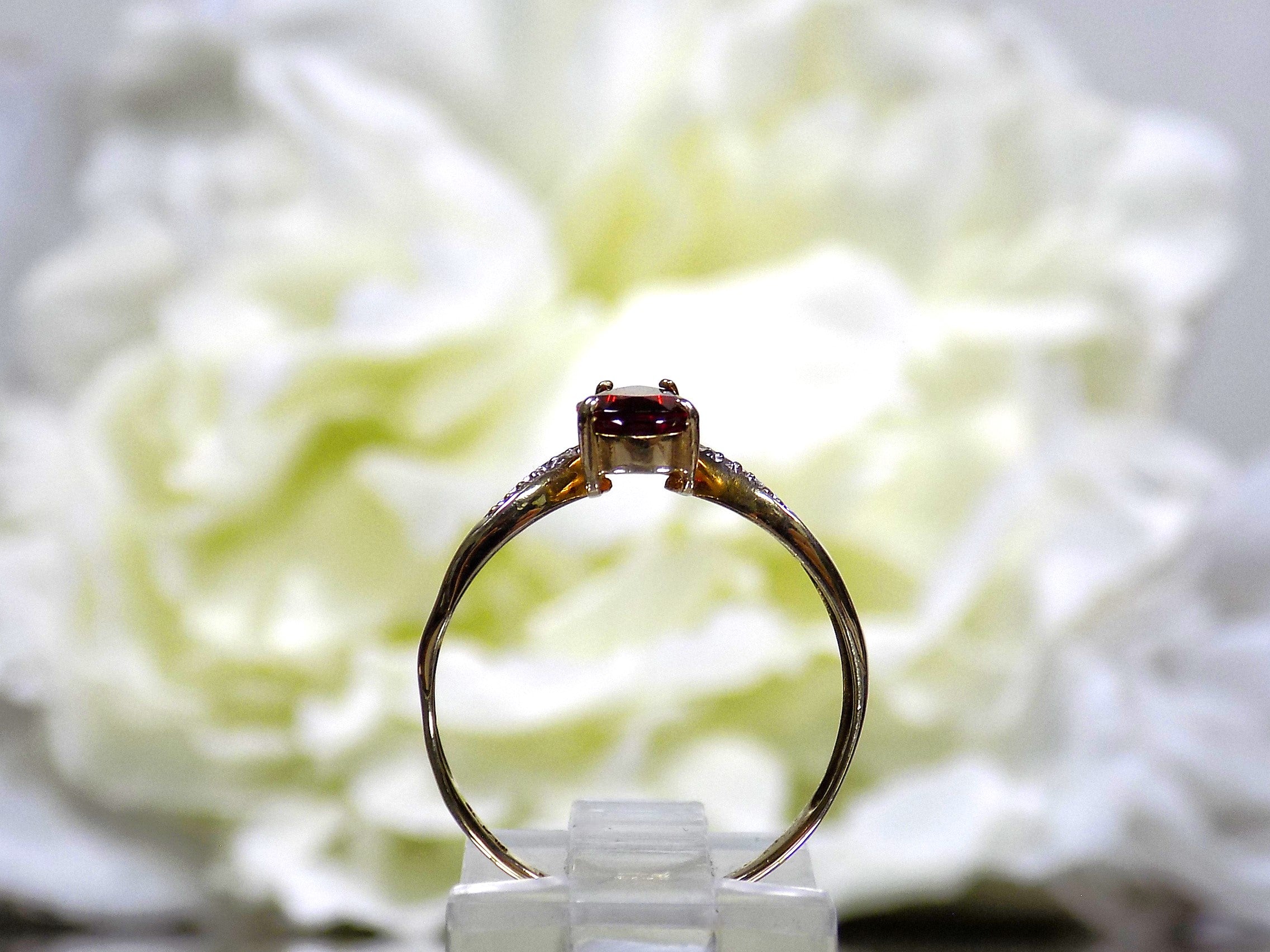 This is a side view pear shape garnet ring with diamond accents in yellow gold with flowery background.